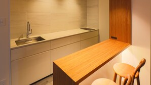 A compact kitchen with a wooden countertop, a sink, and two wooden chairs. - Hotel Muso (Kyoto)
