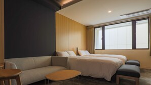 A modern hotel room with a sofa, two single beds, a small table, and a large window providing natural light. - Hotel Muso (Kyoto)