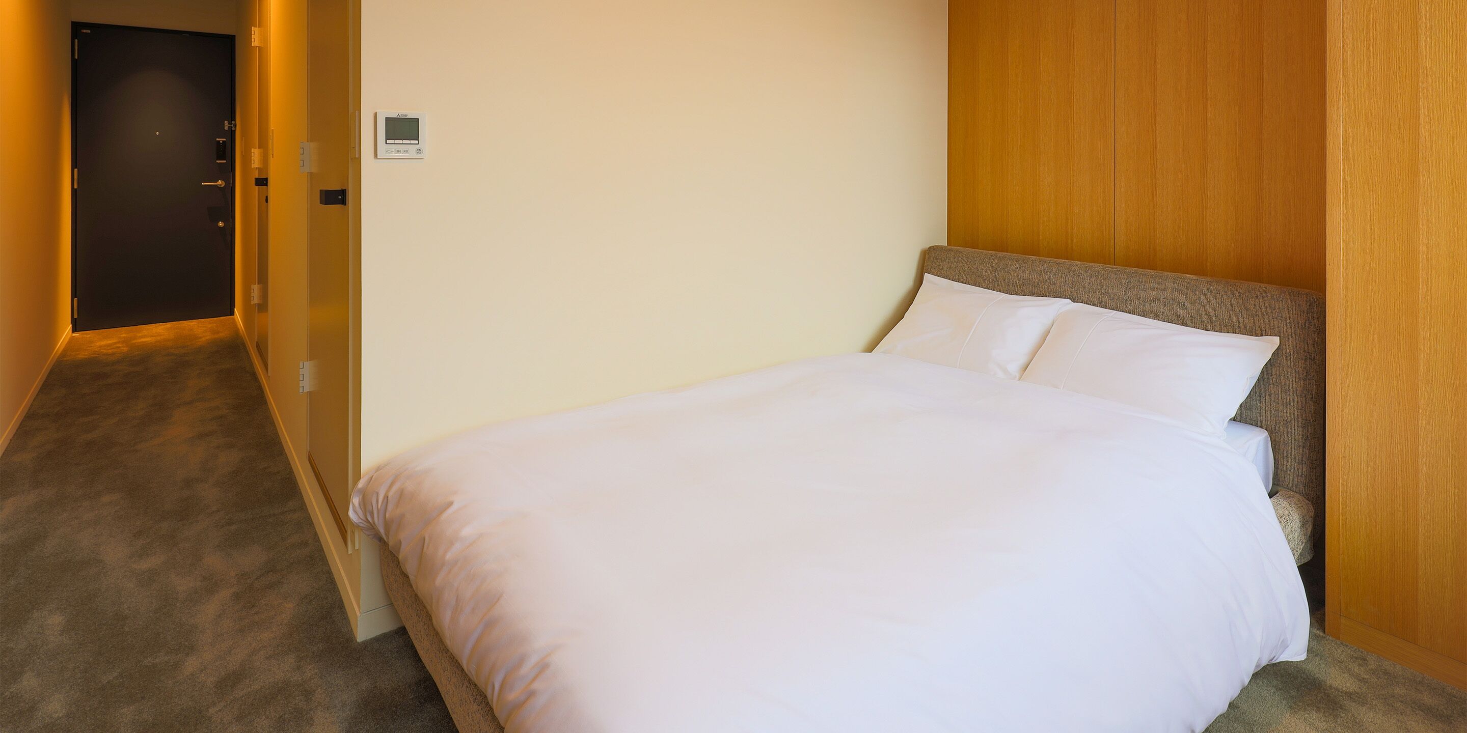 Ein Hotelzimmer mit einem Bett, einem Holz-Kopfteil, Teppichboden und einer Tür.