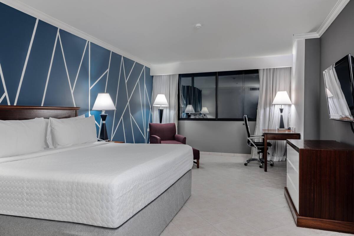 Ein Hotelzimmer mit einem großen Bett, zwei Nachttischen mit Lampen, einem Schreibtisch, einem Stuhl und einem Fernseher.
