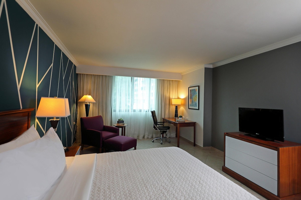 Ein Hotelzimmer mit Bett, Schreibtisch, Stuhl, Fernseher und Lampe.