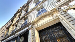 Un bâtiment historique doté d’éléments architecturaux raffinés, notamment une imposante entrée avec un portail en fer forgé noir et de nombreux balcons ornés de garde-corps complexes.