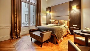 Une chambre d’hôtel avec un grand lit, une petite table, une chaise et une fenêtre avec des rideaux.