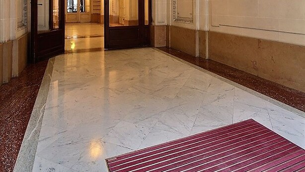 Un vaste hall avec un sol en marbre, un tapis à rayures rouges et un lustre.