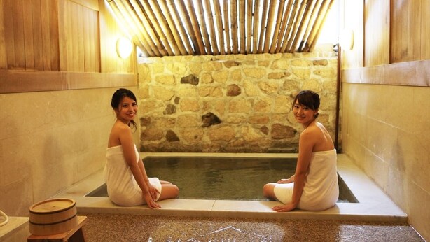 Two people sitting in a stone-walled bathtub with a bamboo ceiling. - OkutsuHotSpa Ikedaya Kajikaen (Kagamino)