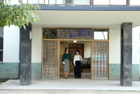 A building entrance with a traditional Japanese gate, a sign above the entrance, and two people standing in the doorway. - OkutsuHotSpa Ikedaya Kajikaen (Kagamino)