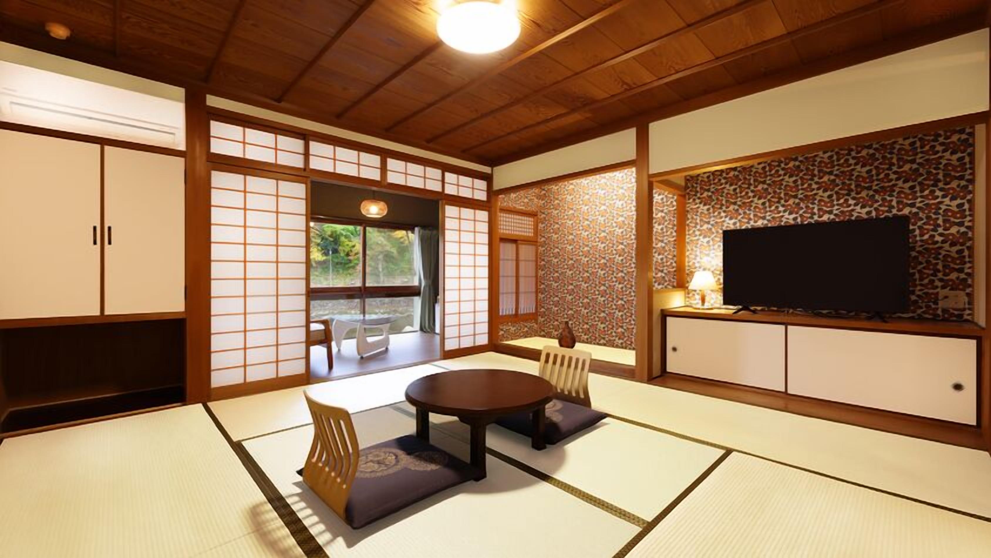 A traditional Japanese room with tatami flooring, a low table with cushions, sliding doors, and a television on a cabinet.