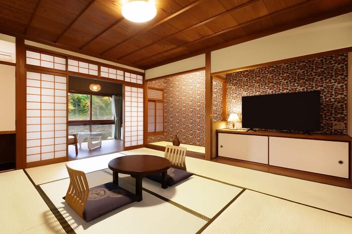 Perinteinen japanilainen huone, jossa on tatamimatto, matala pöytä tyynyineen, liukuovet ja televisio, joka on sijoitettu kaappiin.