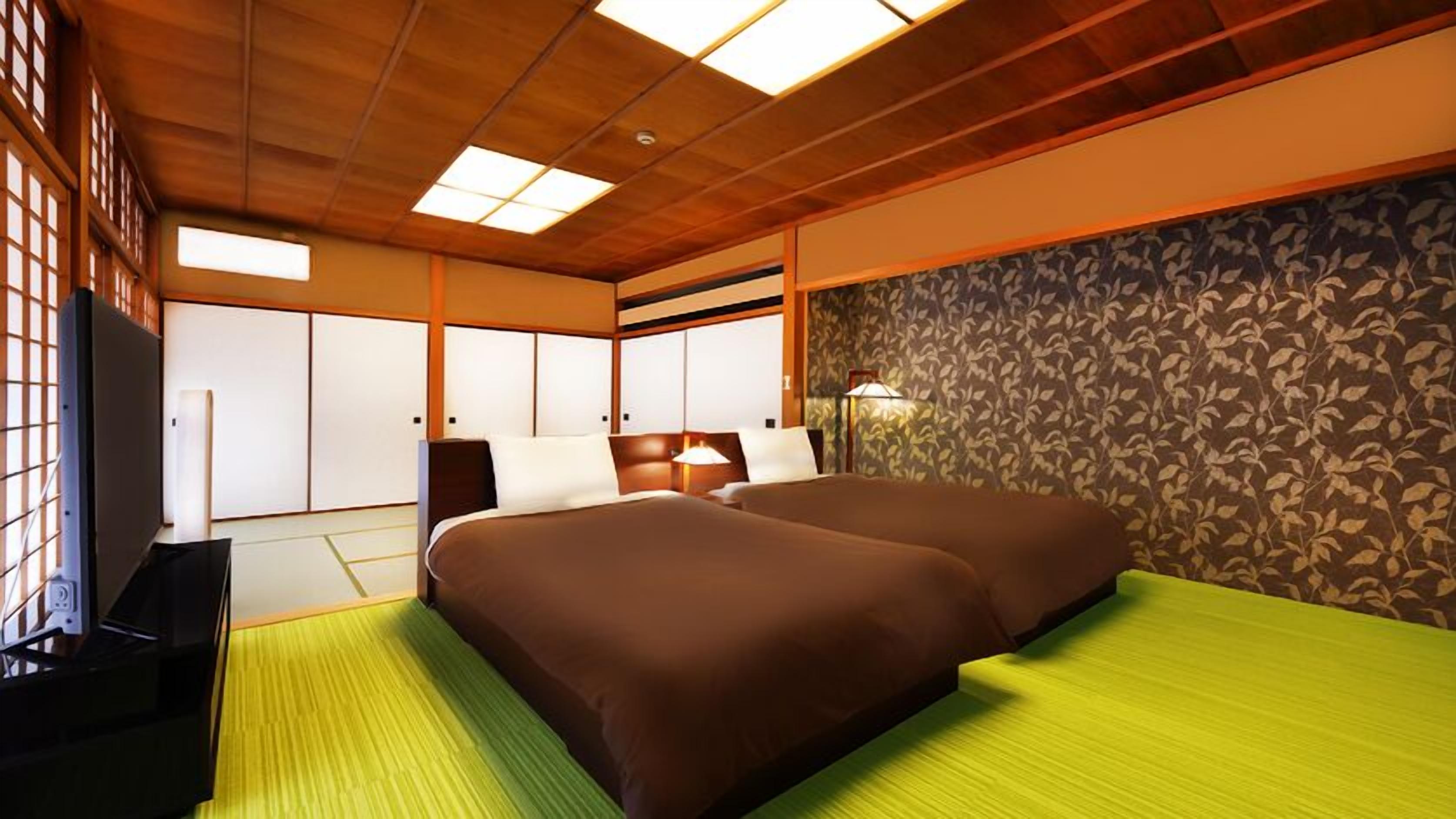 Hotelkamer met een houten plafond, een bed met bruin beddengoed, een groene mat en een televisie, en een behang met een patroon.
