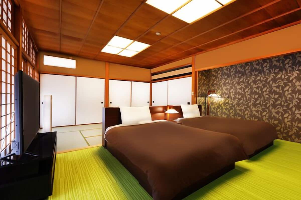 Habitación de hotel con techo de madera, cama con ropa de cama marrón, un tapete verde, televisor y pared con diseño.