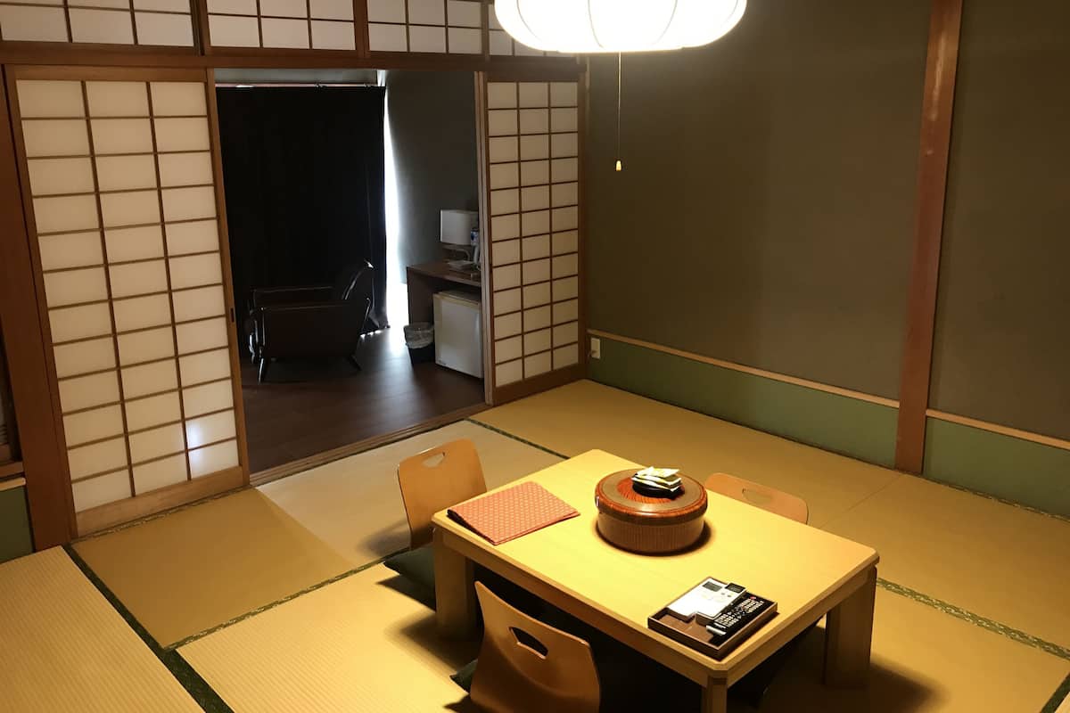 Ett traditionellt japanskt rum med tatamimattor på golvet, ett lågt bord med en dekorativ detalj och skjutdörrar.
