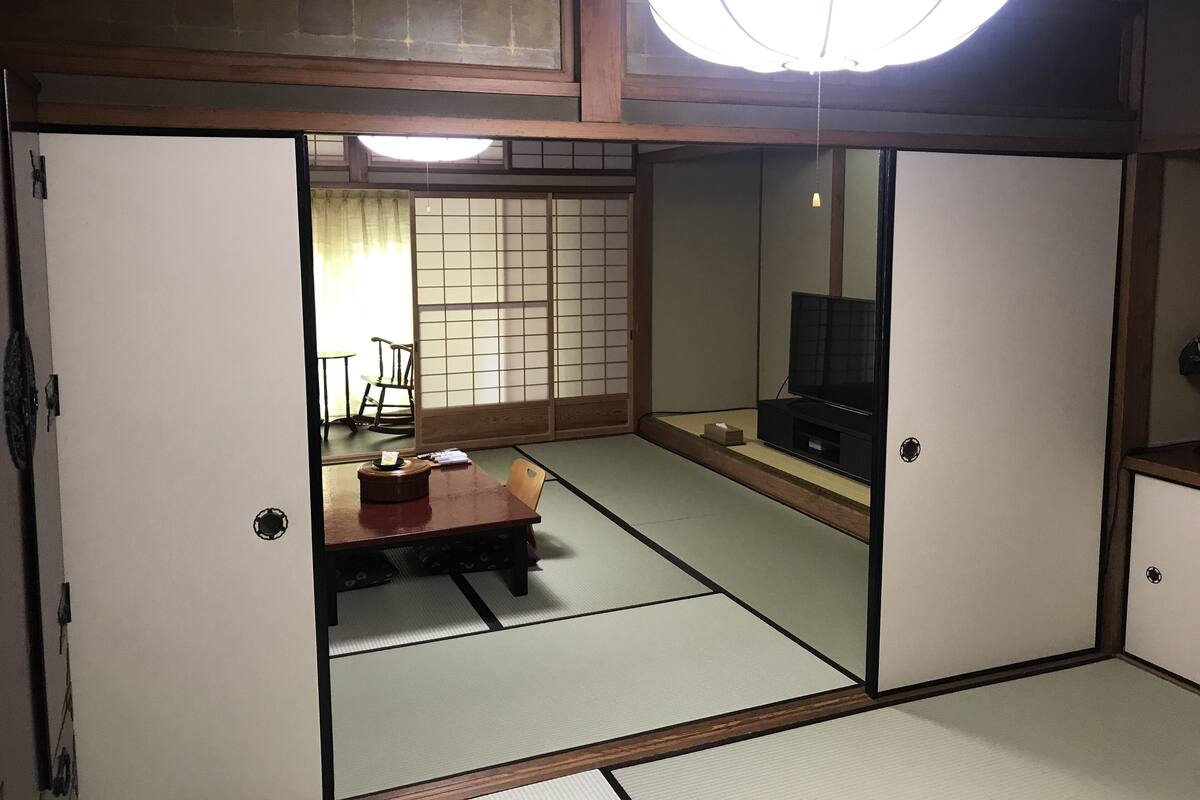 Ett traditionellt japanskt rum med tatamimattor på golvet, ett lågt träbord, en tv och skjutbara shojipaneler.