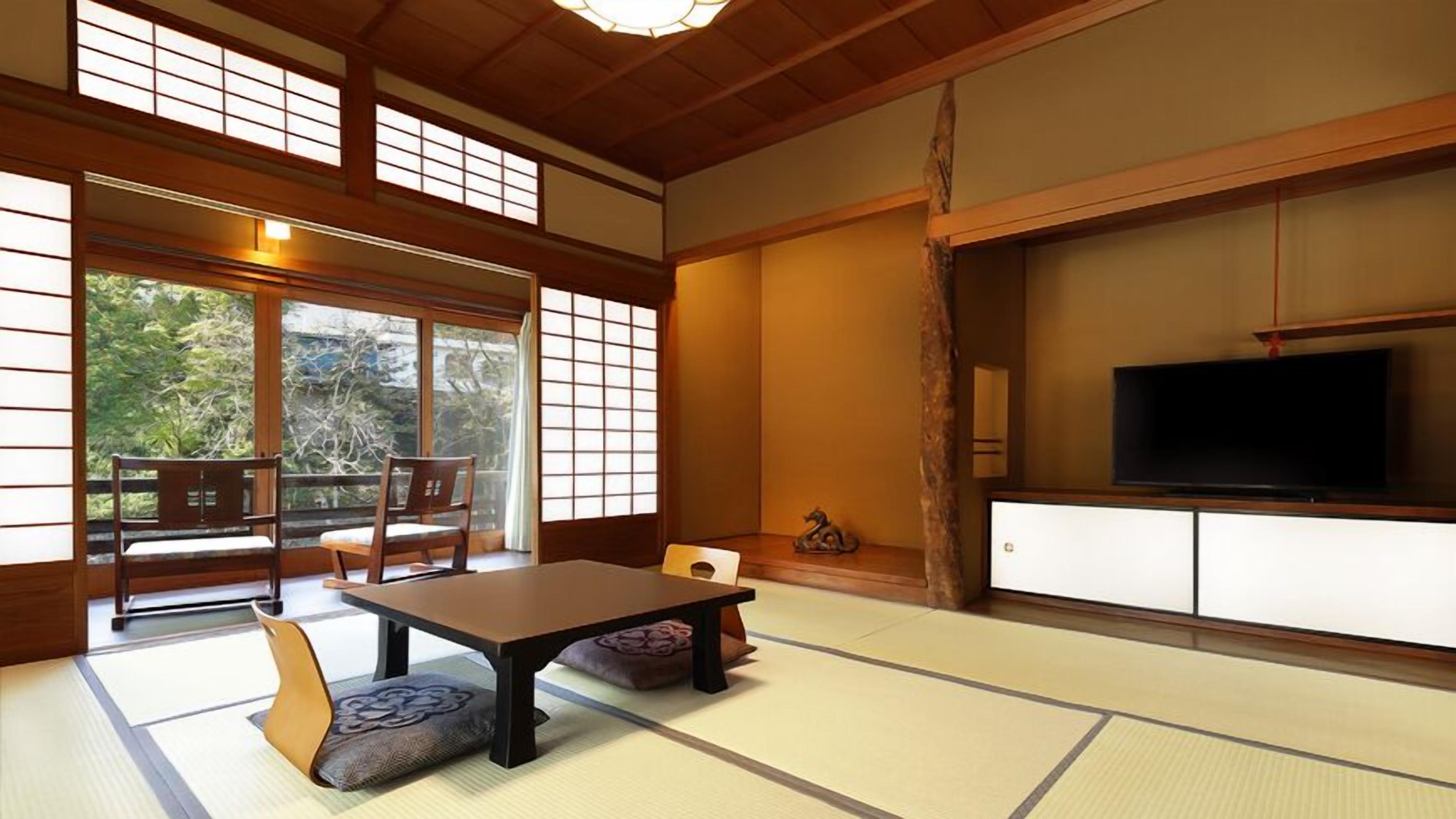 A traditional Japanese room with tatami flooring, a low table, a television, and a sliding door leading to an outdoor area.