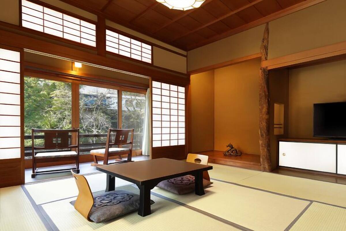 Ett traditionellt japanskt rum med tatamimattor på golvet, ett lågt bord, en tv och en skjutdörr som leder ut till ett område utomhus.