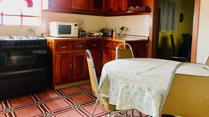 A kitchen with wooden cabinets, a stove, a microwave, a chair, and a table with a floral tablecloth.