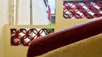 Une vue à travers un portail en métal décoratif orné de motifs géométriques, qui mène à un bâtiment doté d’un toit rouge et d’une fenêtre avec des barreaux en métal.