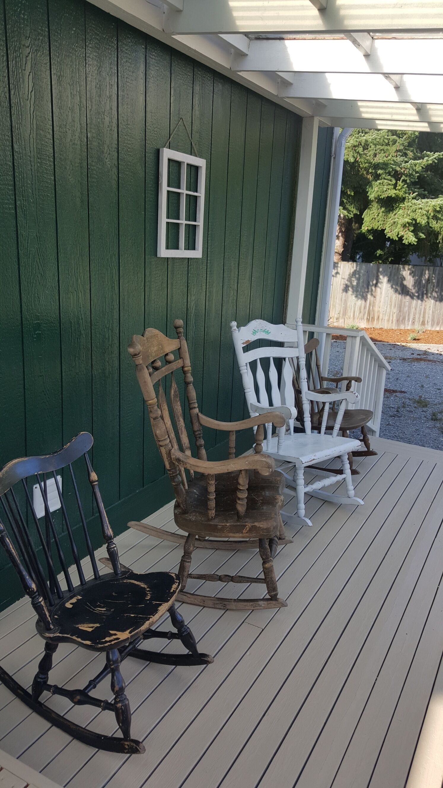 A porch with two rocking chairs, one black and one white, against a green wall.