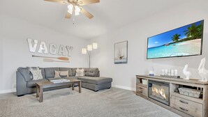 A modern living room with a grey sofa, a wooden coffee table, a fireplace, and a large TV screen displaying a beach scene.