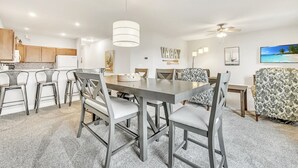 A modern kitchen with wooden cabinets, a dining area with a large table and chairs, and a ceiling fan.