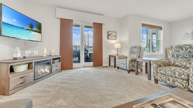 A spacious living room with a fireplace, a large TV, and a view of the outdoors through a sliding glass door.