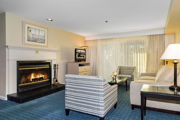 A living room with a fireplace, a television, a patterned armchair, a sofa, and a lamp.