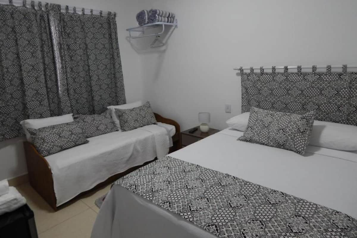 Un dormitorio con dos camas, ropa de cama estampada, una mesita de noche con lámpara y un estante en la pared con una toalla.