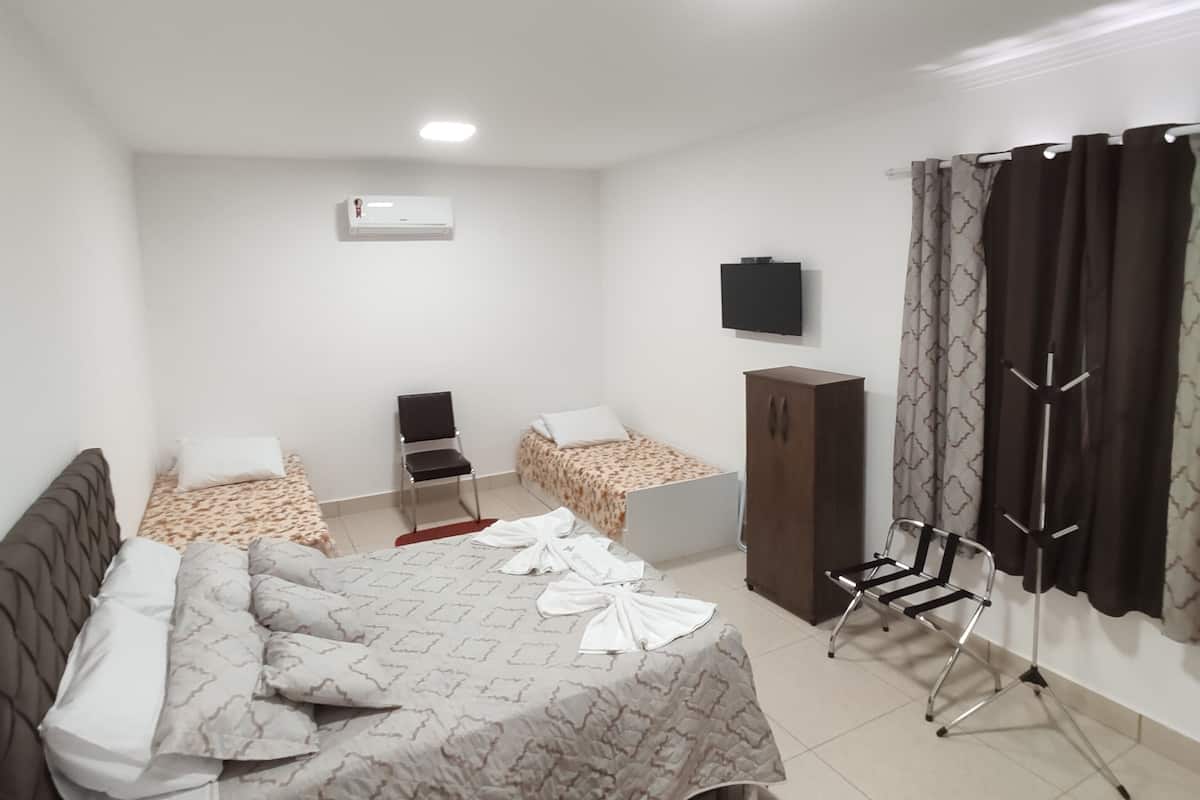 Un dormitorio con cama, escritorio, silla, aire acondicionado, armario y televisor en la pared.