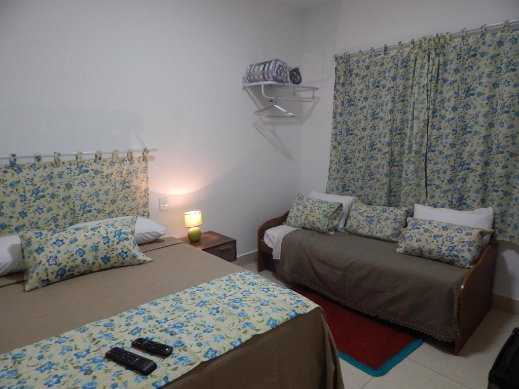 A bedroom with two beds, a nightstand, a wall-mounted shelf, and a window with curtains.
