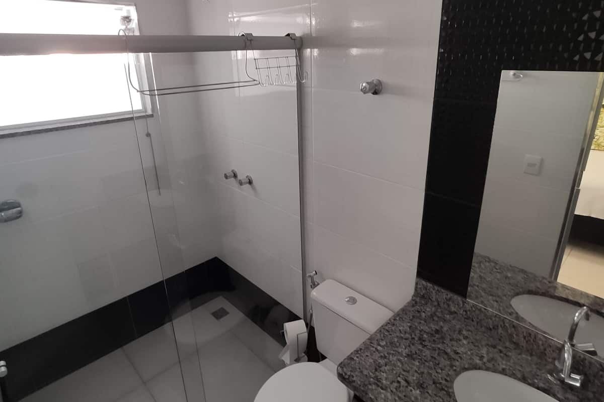 Un baño moderno con cabina de ducha de vidrio, inodoro y encimera de granito con lavamanos.