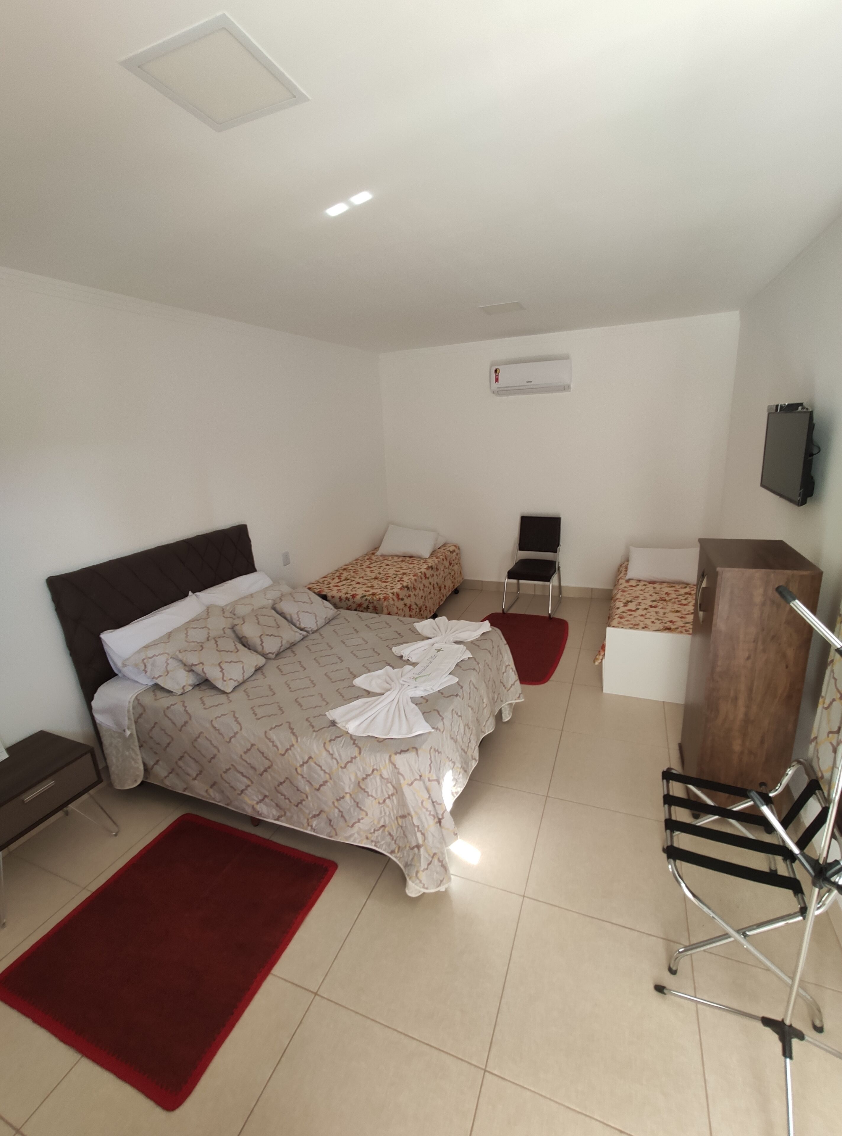 A hotel room with a large bed, a desk, a chair, a TV, and an air conditioning unit.