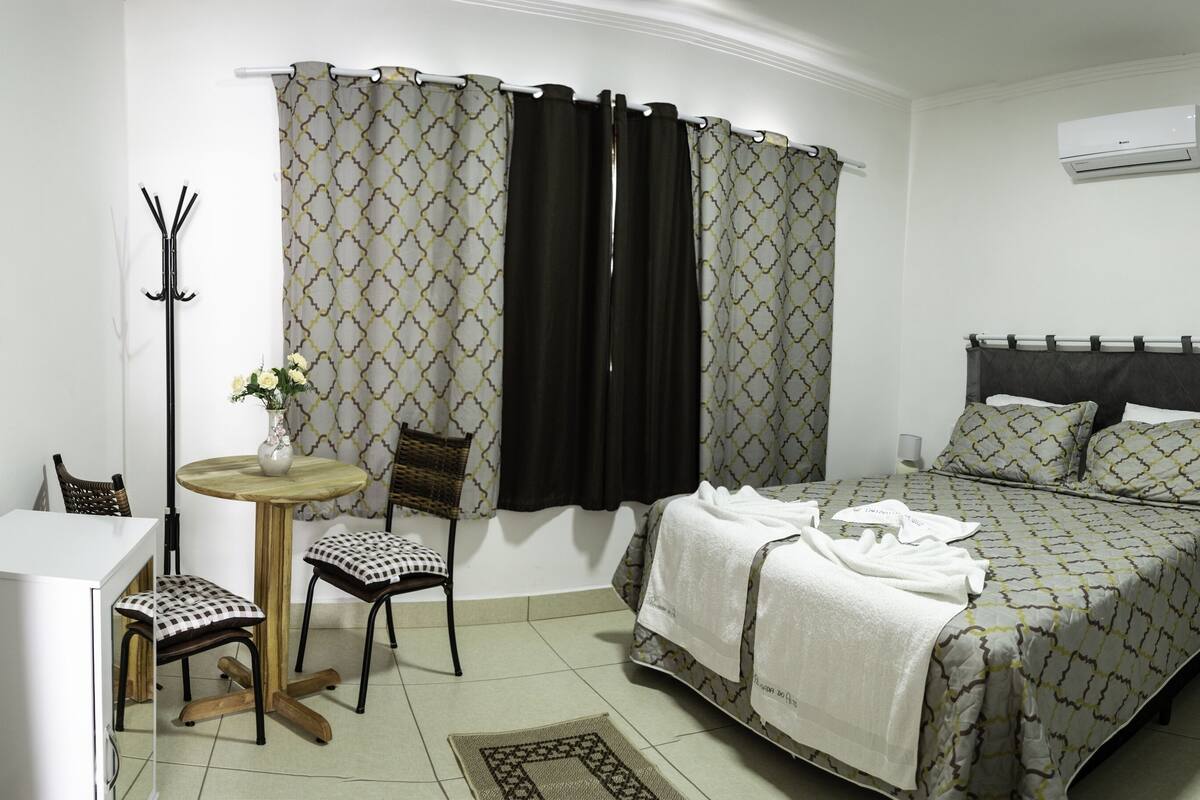 Un dormitorio con cama, una silla, una mesita y un perchero.