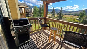 Eine Holzterrasse mit Grill, zwei Stühlen und einem Tisch.