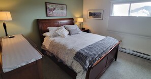Un lit bien fait, avec une couvre-lit à motifs et des oreillers, une table de chevet avec une lampe et une fenêtre avec des stores.