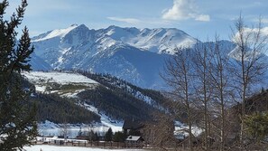 Un paysage montagneux aux sommets enneigés, une zone boisée et un petit bâtiment doté d’une courClose.