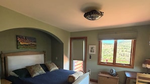 A bedroom with a bed, a desk, a chair, a fan, and a window with a view.