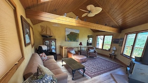 A spacious living room with a high ceiling, wooden beams, a large window, a fireplace, and a cozy seating area.