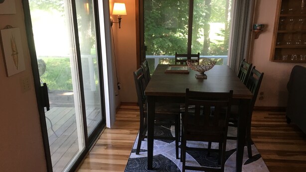 A dining area with a table, chairs, a rug, and a window with a view of greenery.