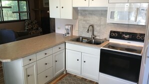 A compact kitchen with white cabinets, a stainless steel sink, a built-in microwave, and a stove.