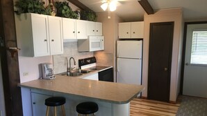 A kitchen with white cabinets, a stainless steel sink, a stove, and a refrigerator. There are two wooden stools at the island.