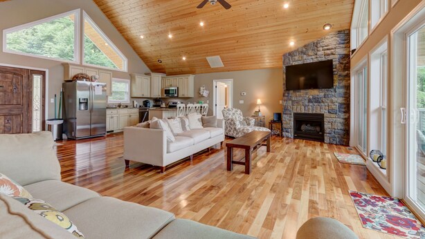 A spacious living room with a wooden ceiling, a stone fireplace, and a large window overlooking the outdoors.