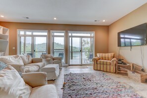Relax in this spacious living room with a large sofa, flat-screen TV, and sliding glass door leading to a balcony with a lush view.
