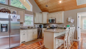 A modern kitchen with wooden ceiling, stainless steel appliances, and a central island with bar stools. - Waterfront, 2025 Tram, 2023 Dock, Sleeps 14, 3BR, 3.5 Bath, Wifi @ House & Dock (Jacksboro)