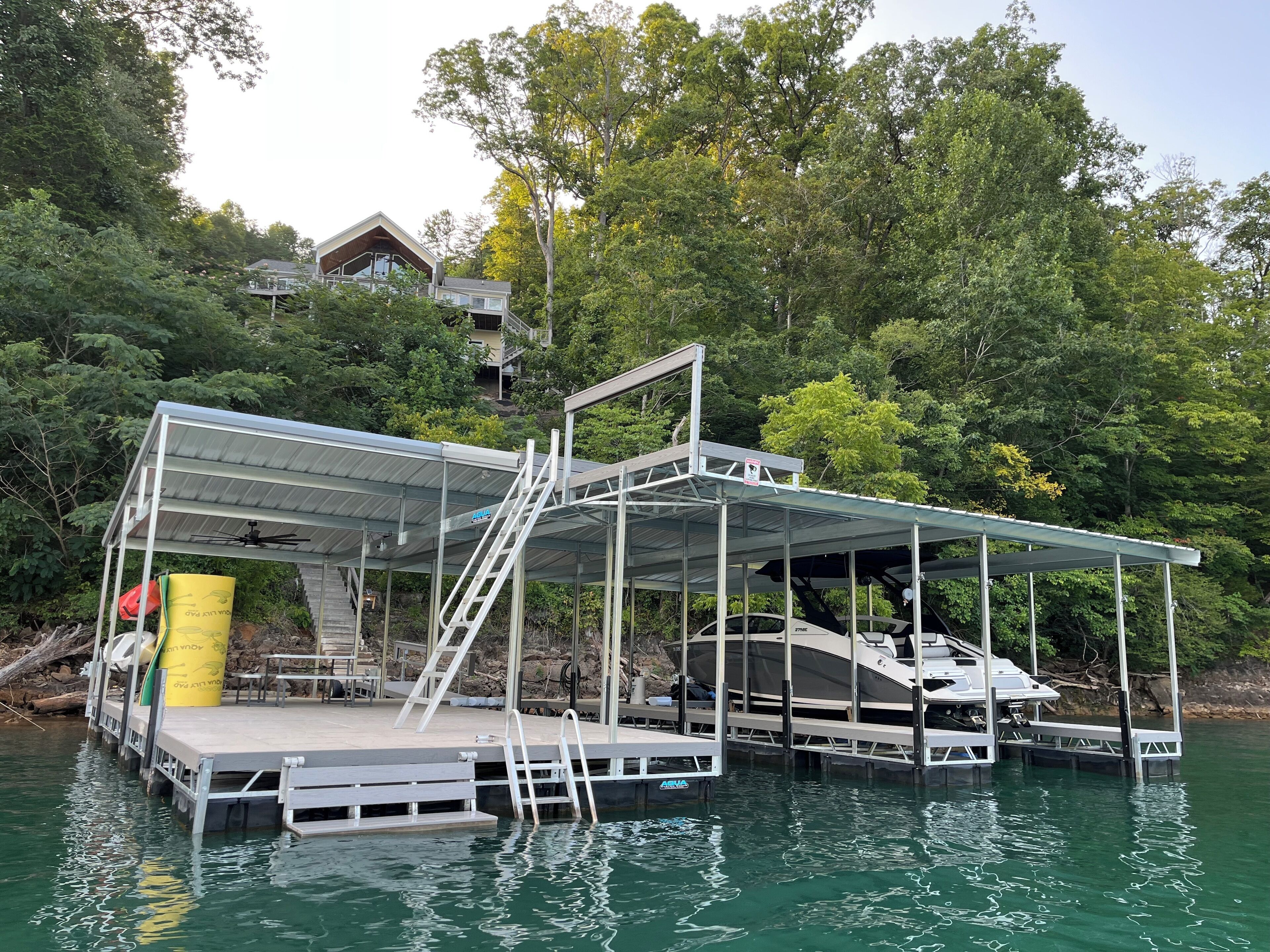 A dock with a covered area, a boat, and a house in the background.
