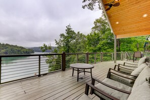 Relax on the deck with a view of the calm lake and lush greenery, surrounded by comfortable seating and a railing for a safe and unobstructed view.