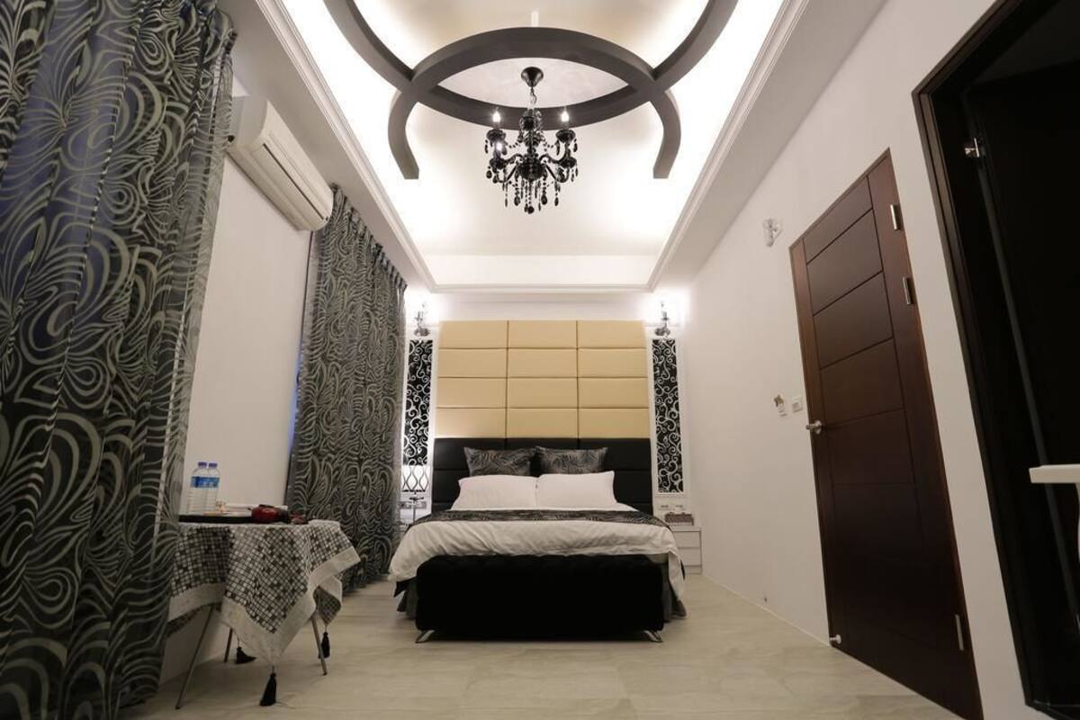 Un dormitorio con cama, lámpara de araña, mesita de noche y cortinas estampadas.