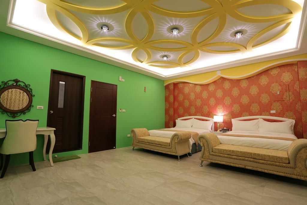 A hotel room with a green wall, a patterned red wall, two beds, a small table, and a chair.