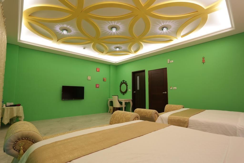 A hotel room with green walls, a decorative ceiling, two beds, a desk, and a television.