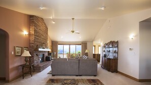 A spacious living room with a fireplace, a large sofa, a patterned rug, and a ceiling fan.