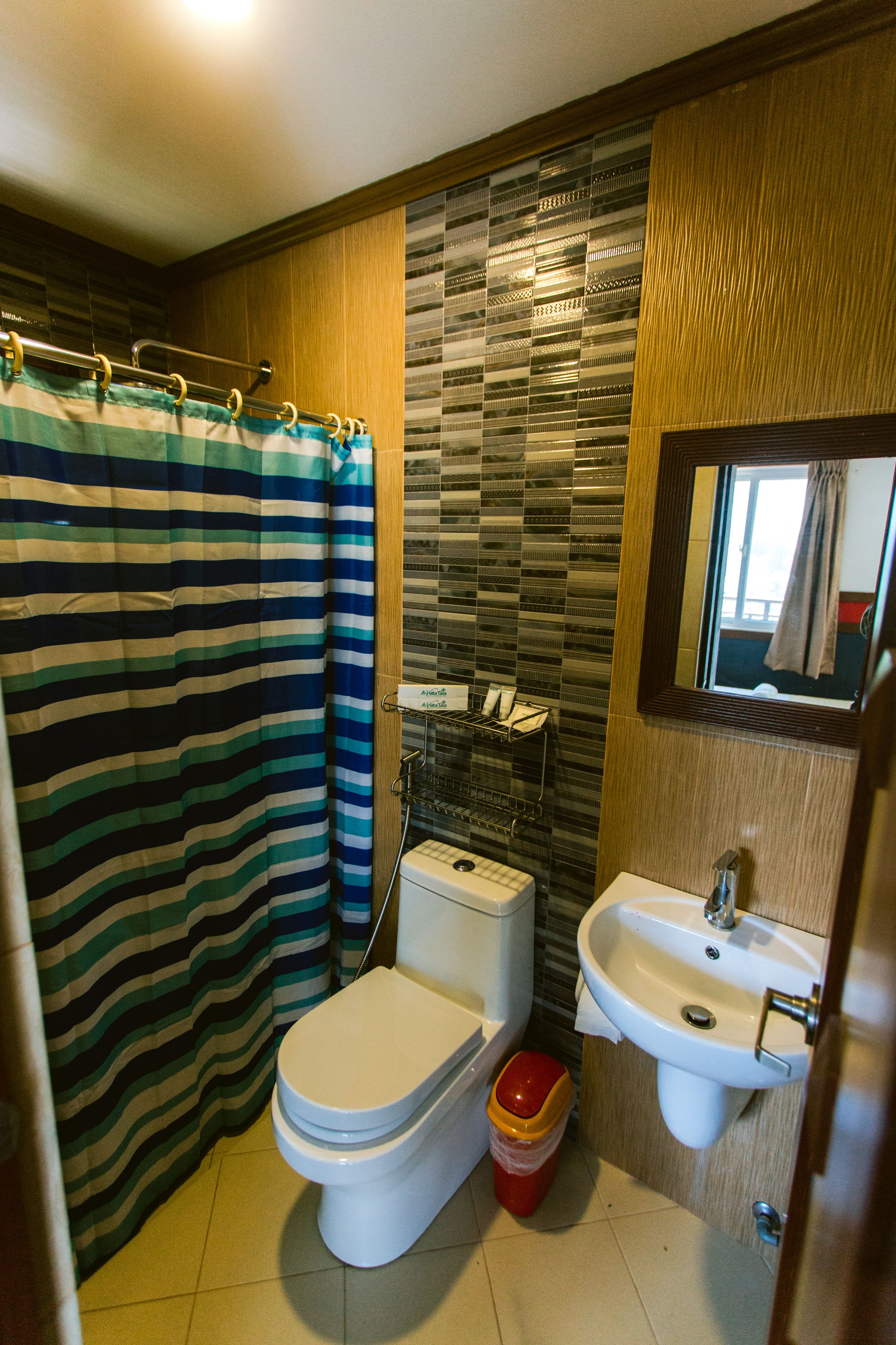 A bathroom with a striped shower curtain, a toilet, a sink, and a trash bin.