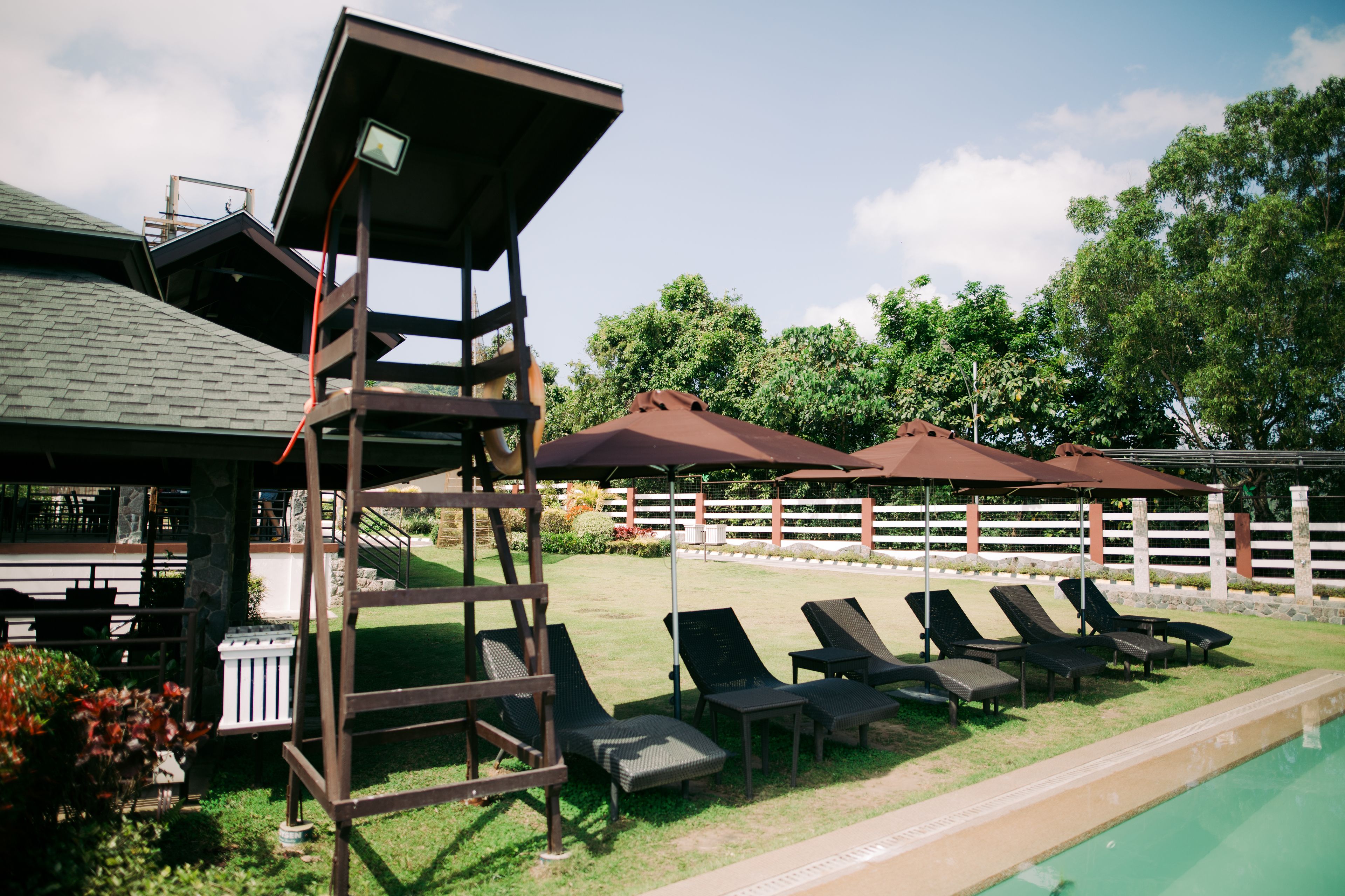 A pool area with lounge chairs and umbrellas, a wooden deck, and a building with a sloped roof.